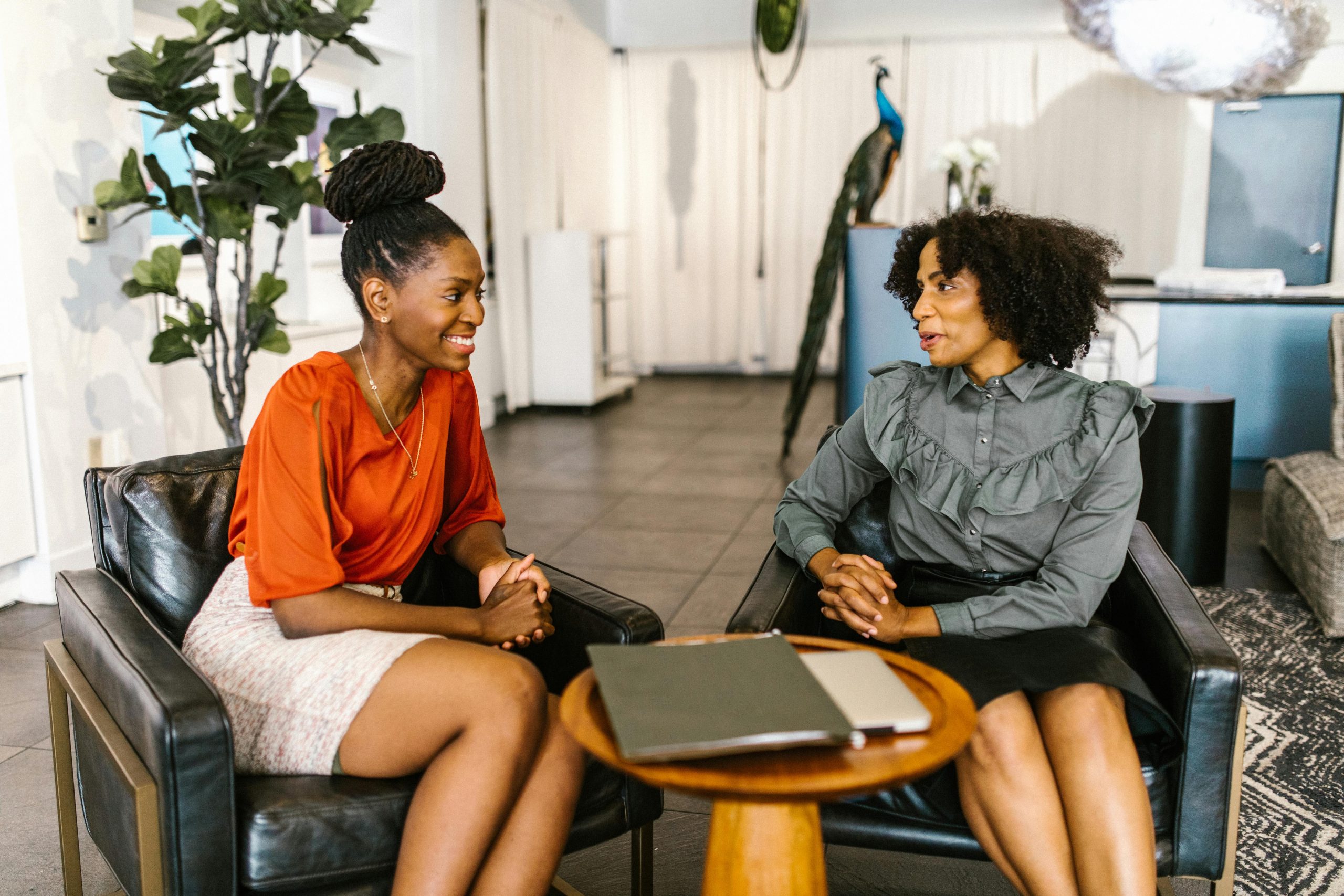 Two professional women sitting in a modern office setting, engaged in a friendly conversation.